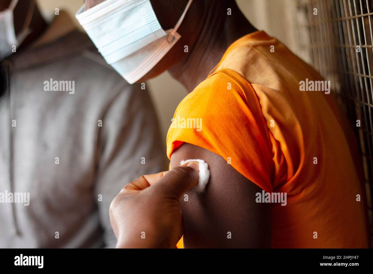 A health worker prepares a patient's arm, cleaning with cotton wool dipped in disinfectant to prepare for Covid-19 vaccination. Malawi. Stock Photo
