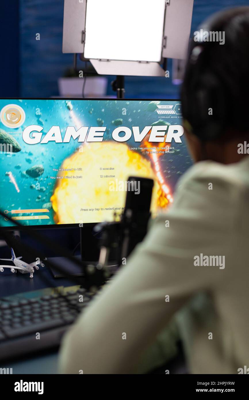 Sad upset esport gamer sitting at gaming desk playing space shooter videogames losing online games championship. Nervous woman streaming live using RGB computer equipment, Game over on screen Stock Photo