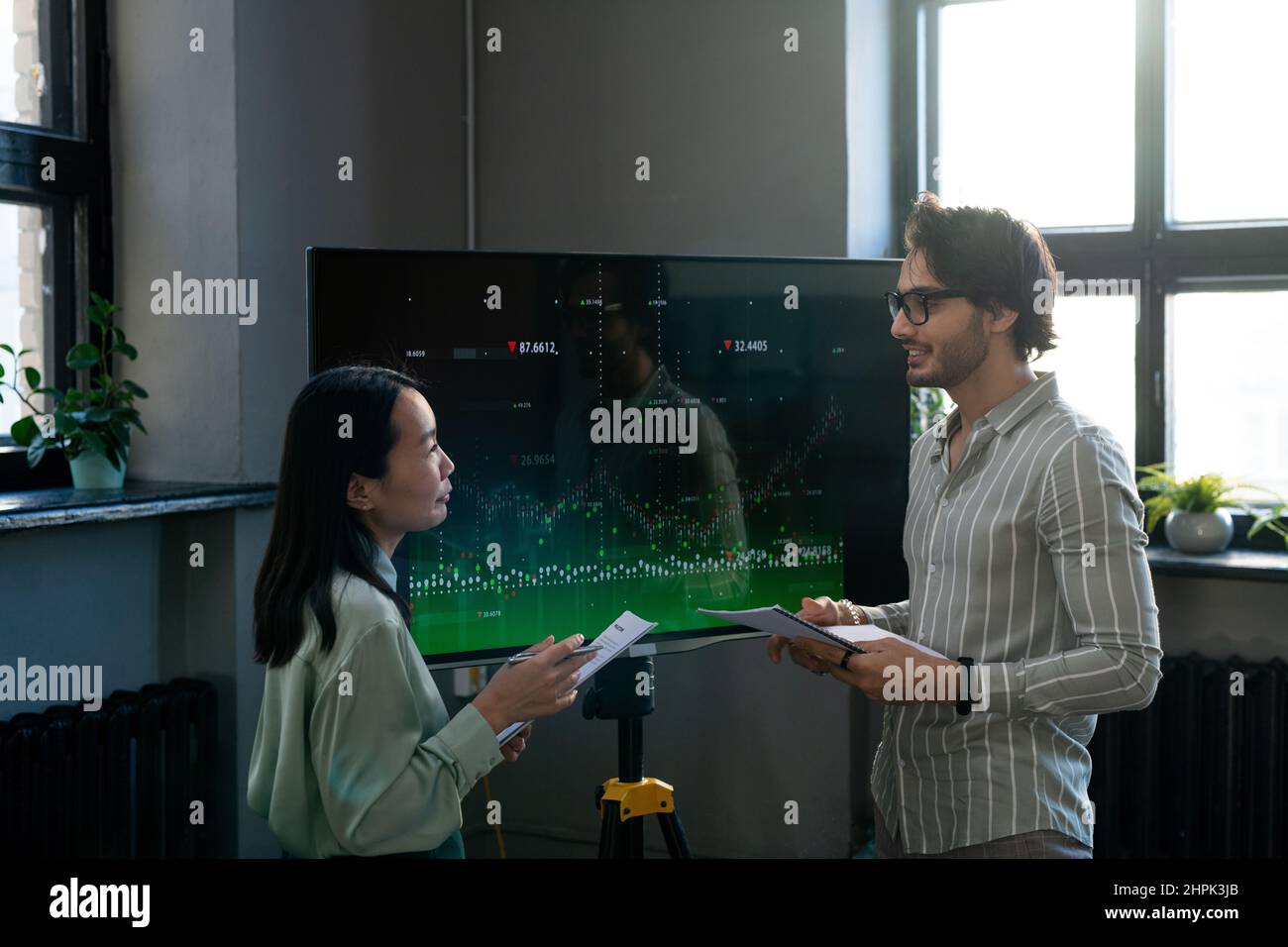 Two young confident analysts with documents discussing interactive financial data while businessman explaining something to female colleague Stock Photo