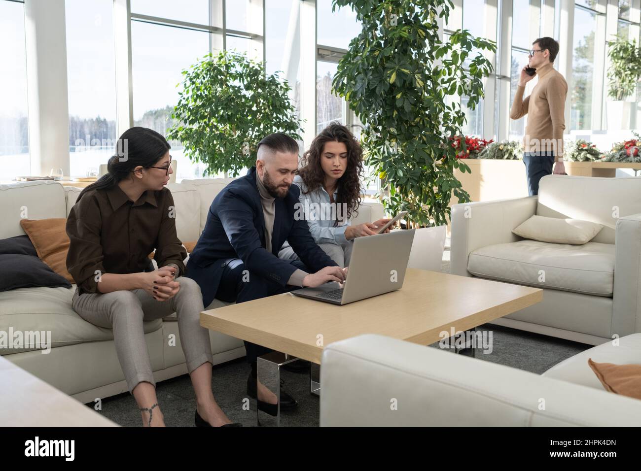 Three managers of modern high tech corporation brainstorming while analyzing online technology data by table against their colleague Stock Photo