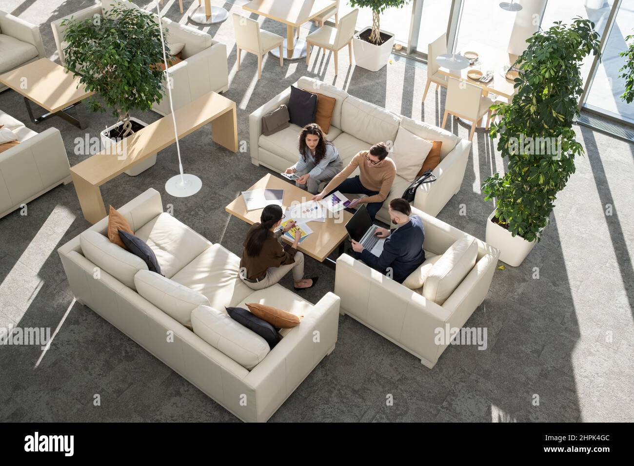 Group of young auditors of high tech corporation discussing documents with data and analyzing it while gathered around table in office Stock Photo