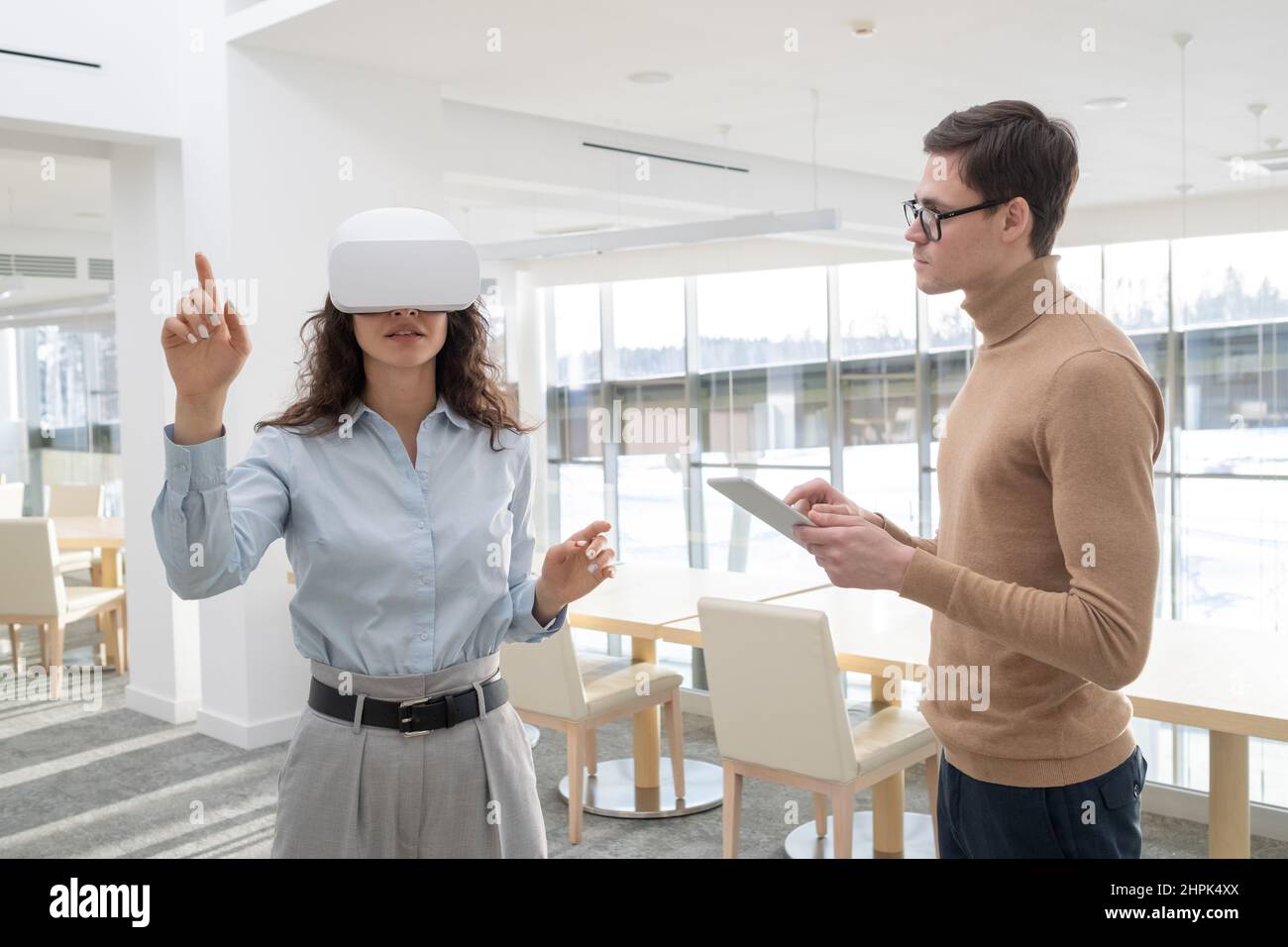 Young female developer of metaverse making presentation of new project to colleague with tablet entering information in electronic database Stock Photo