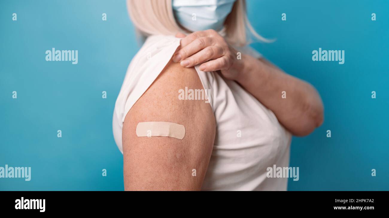 Vaccine and old elder people inoculation. Healthy mature older senior 50s woman in protective medical mask showing arm with plaster after receiving Stock Photo