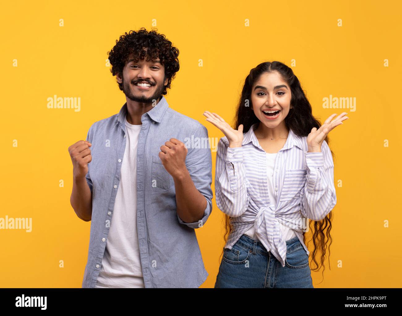 Wow. Overjoyed indian spouses gesturing in amazement looking at camera over yellow studio background Stock Photo