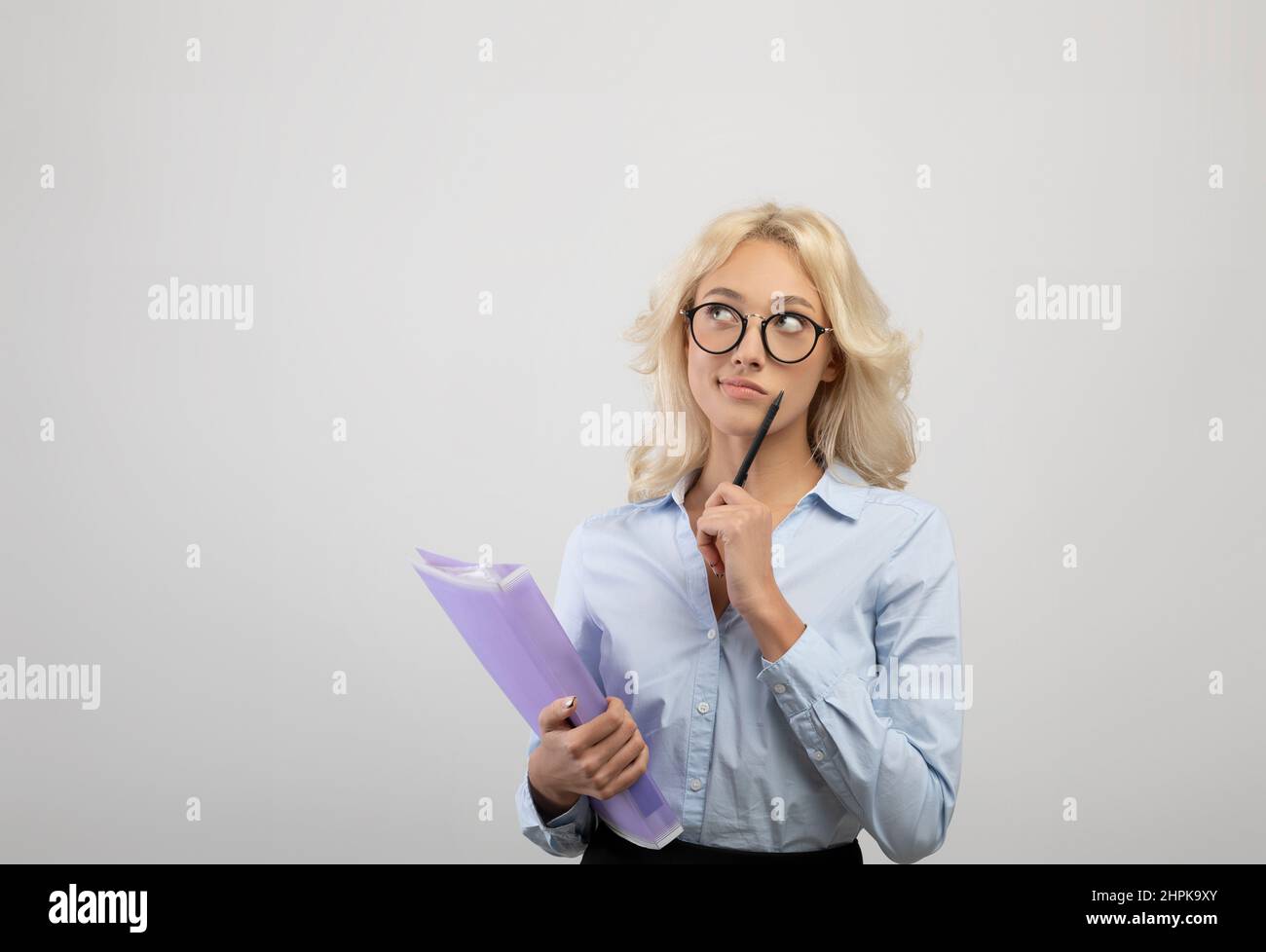 Young dreamy businesswoman holding folder with documents, thinking and looking aside at copy space, light background Stock Photo