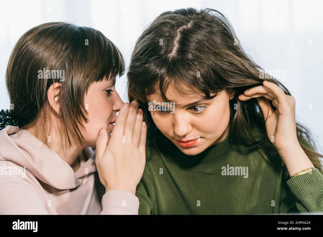Young cute woman whispering secret on ear to her female friend. Communication and surprised girl by gossip. Stock Photo
