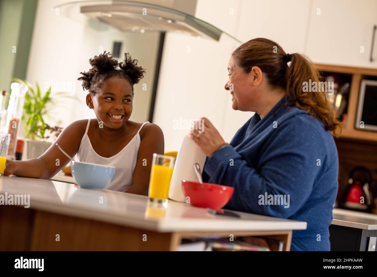 Smiling african american girl looking at happy caucasian mature mother while having breakfast Stock Photo