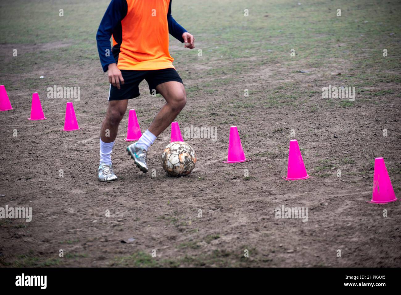 Footballer dribbling ball during training between cones. Young soccer