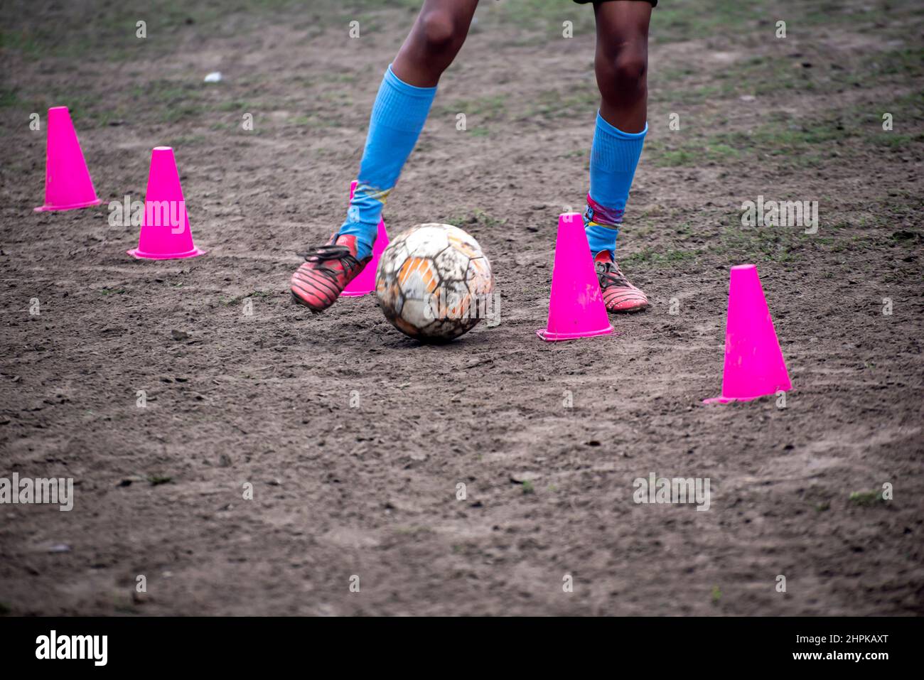 Footballer dribbling ball during training between cones. Young soccer