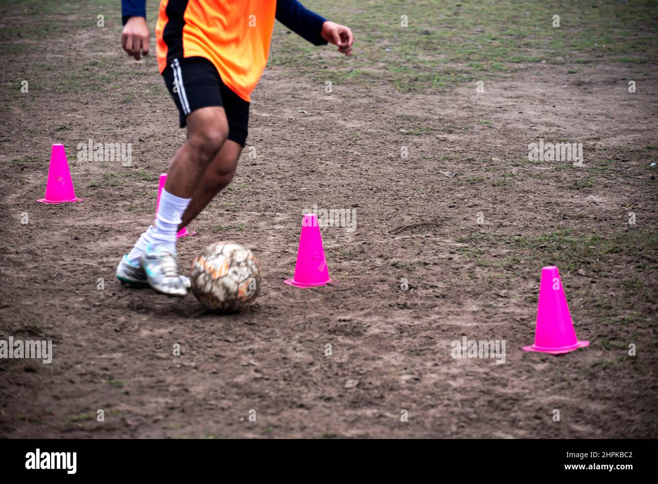 Footballer dribbling ball during training between cones. Young soccer
