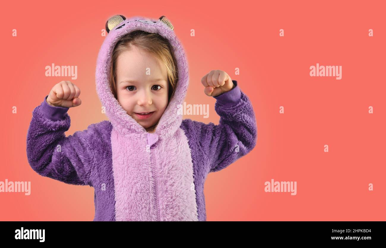 little girl child shows strong strength tensing muscles in purple pajamas Stock Photo