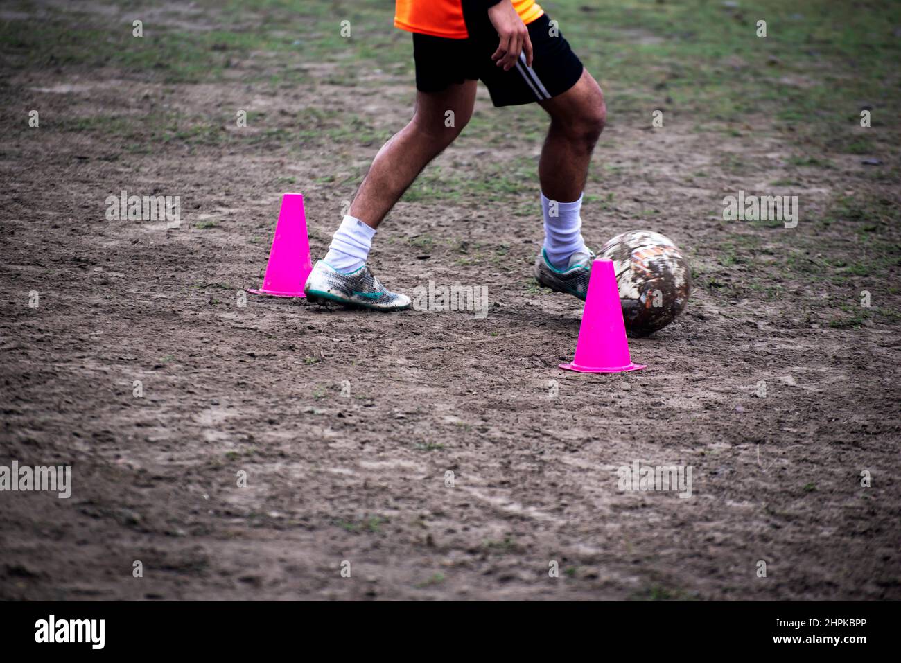 Footballer dribbling ball during training between cones. Young soccer