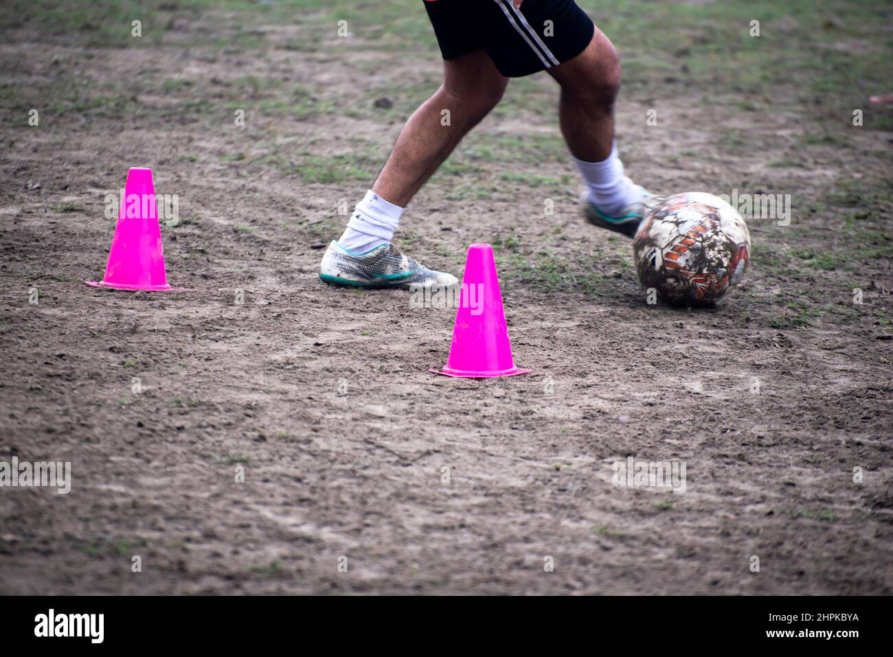 Footballer dribbling ball during training between cones. Young soccer