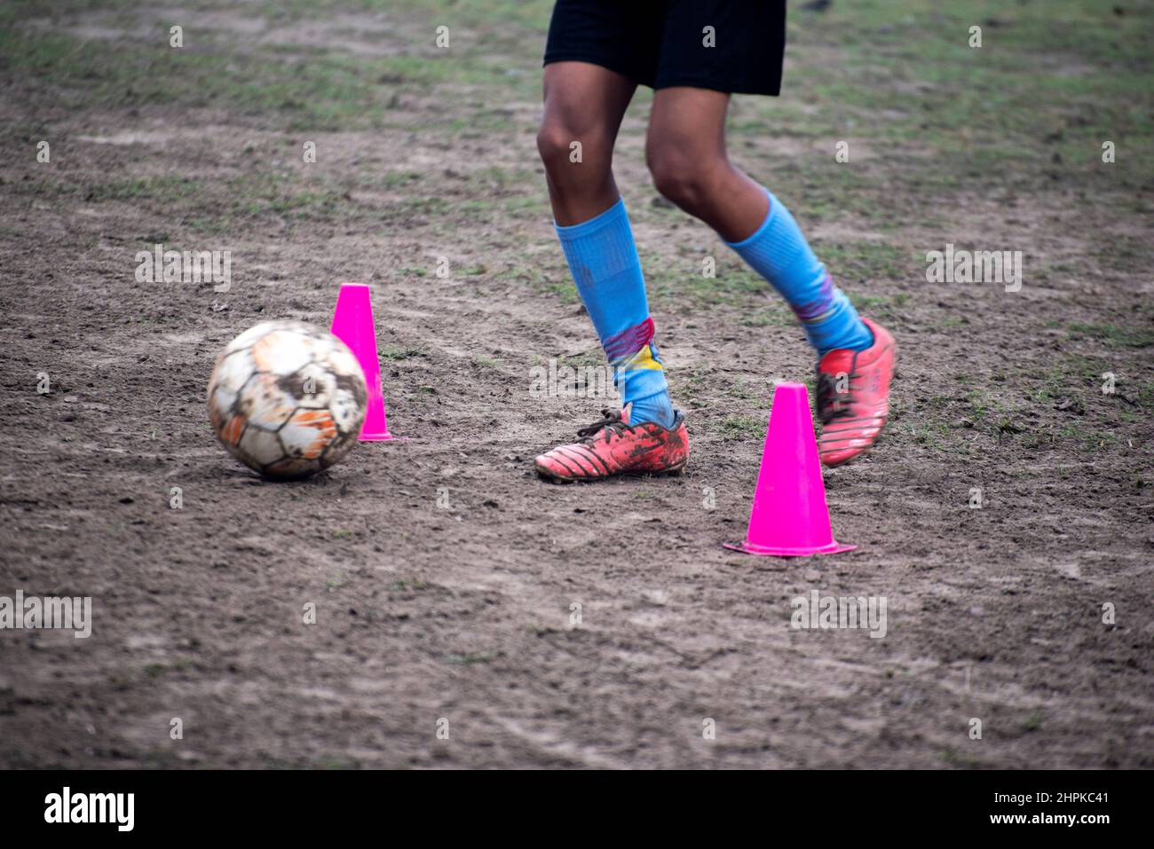 Footballer dribbling ball during training between cones. Young soccer