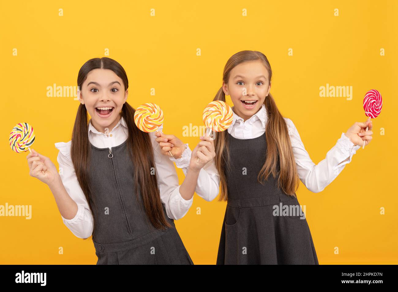 Happy kids in formal uniforms hold lollipops sweet treats yellow background, cheer Stock Photo