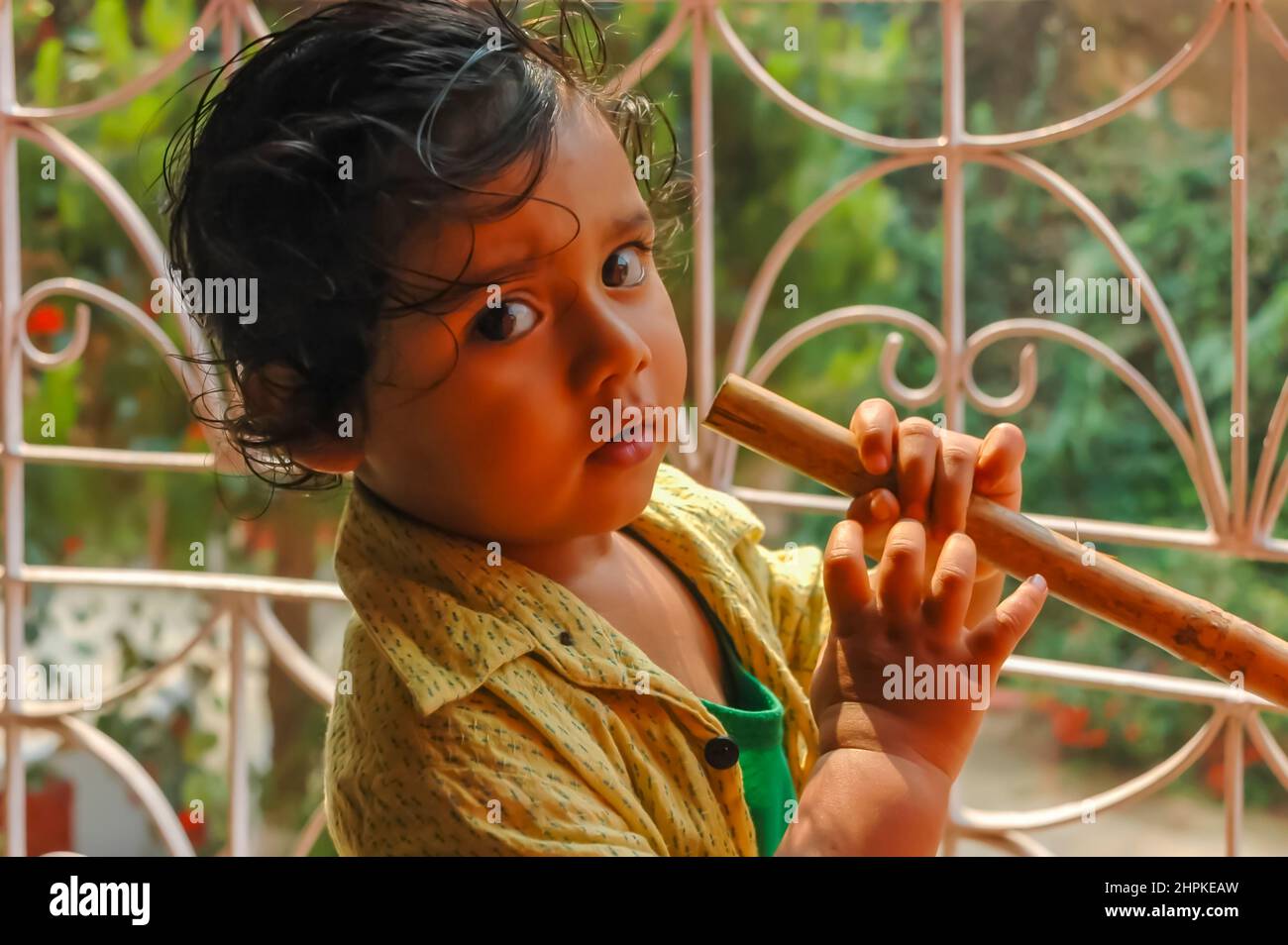 A portrait of an East Indian baby boy / child / kid with an unbuttoned shirt looking askance at the camera with his dark black eyes. Stock Photo