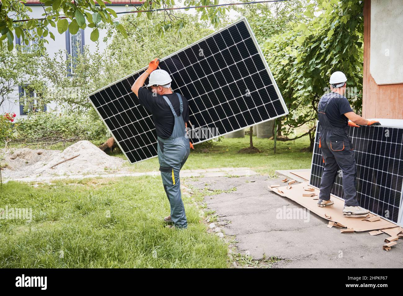Full length of two men in safety helmets carrying solar modules in the ...
