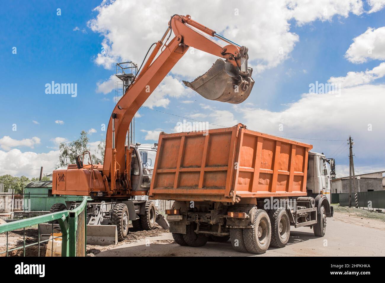 Excavation works. The bucket of the tractor loads the soil with a shovel into the back of a dump truck on the construction site. Stock Photo