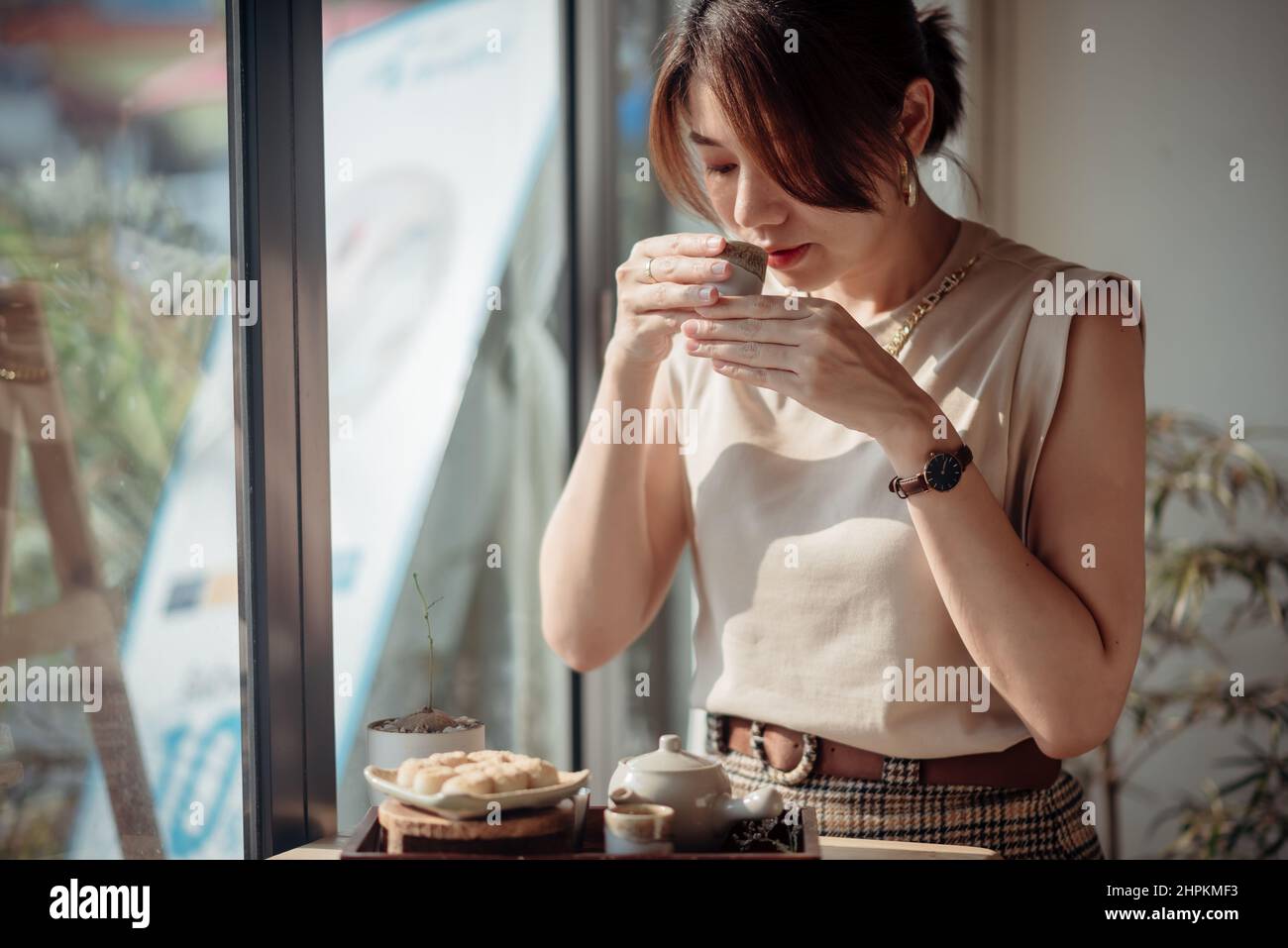 An Asian woman is sniffing tea and has a set of Roasted Mitarashi Dango in front of her. Stock Photo