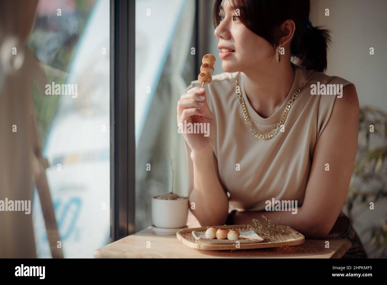 An Asian woman is tasting a Roasted Mitarashi Dango. Stock Photo