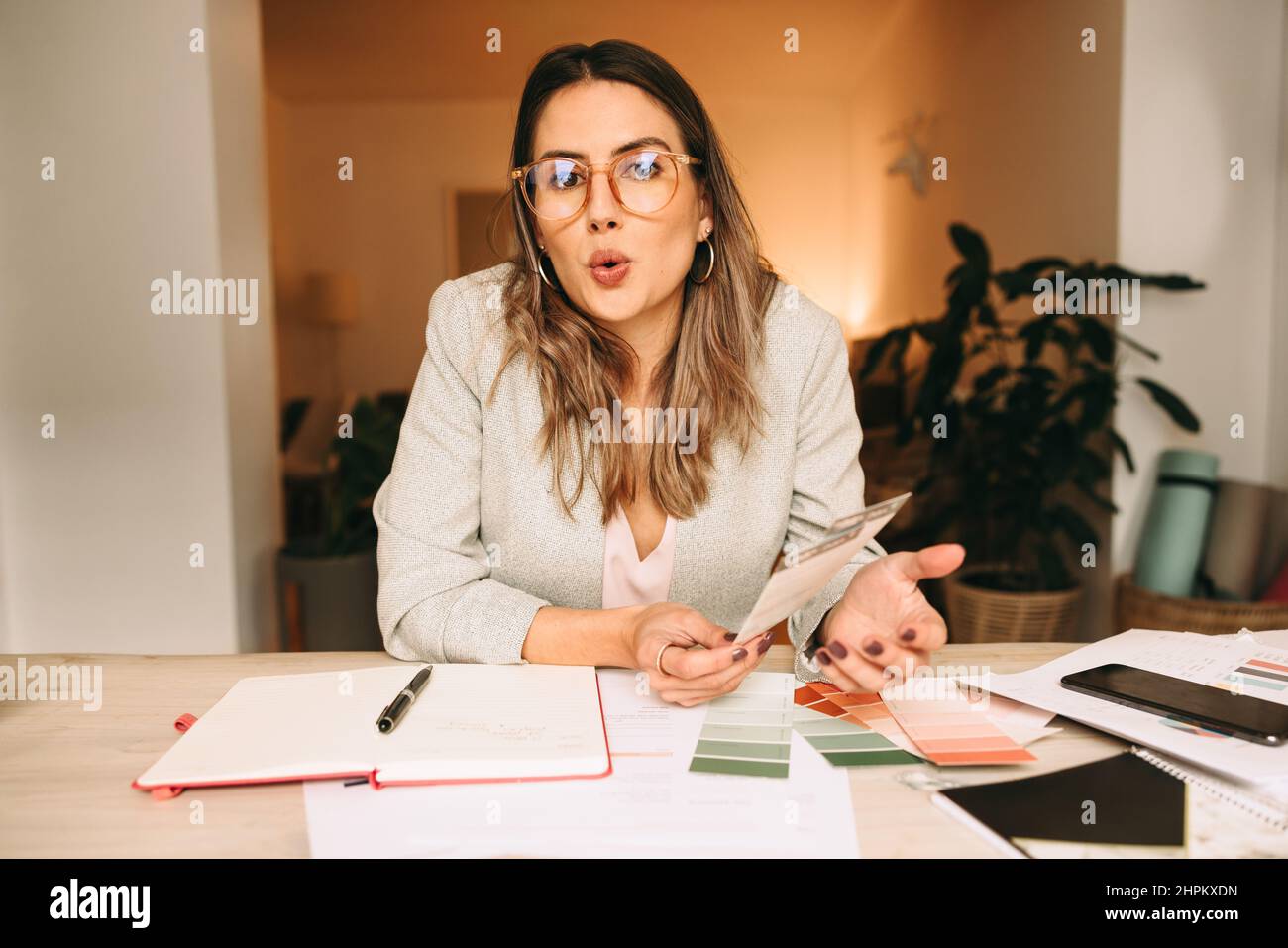Interior designer speaking during a virtual meeting. Creative businesswoman giving an explanation while holding colour swatches. Female designer video Stock Photo