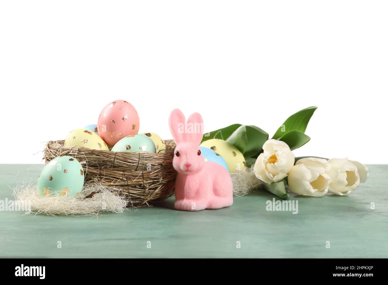 Nest with painted Easter eggs, tulip flowers and bunny on table against ...