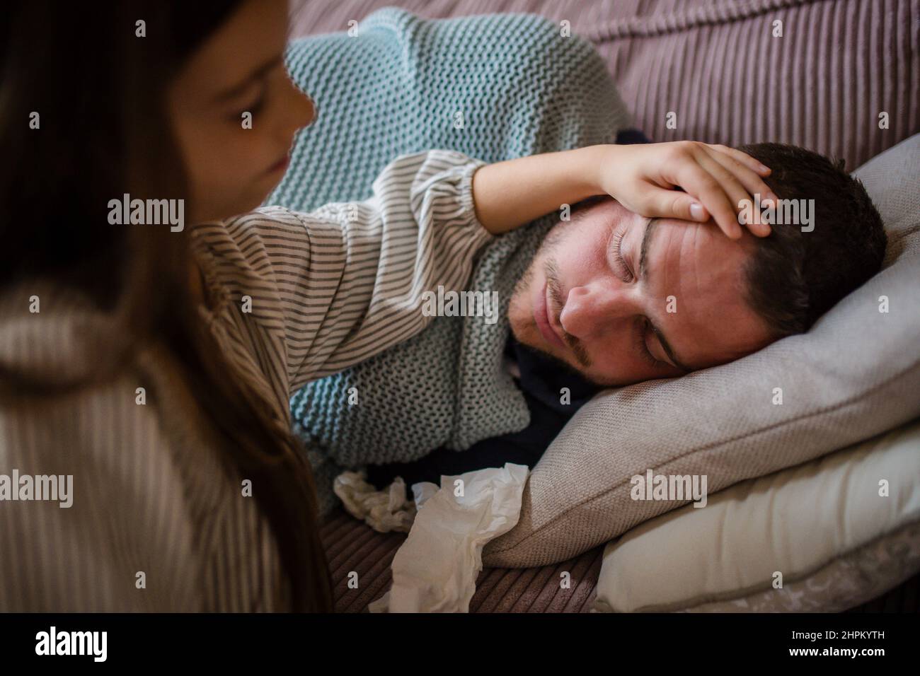 High angle view of little daughter taking care of her sick father at home. Stock Photo