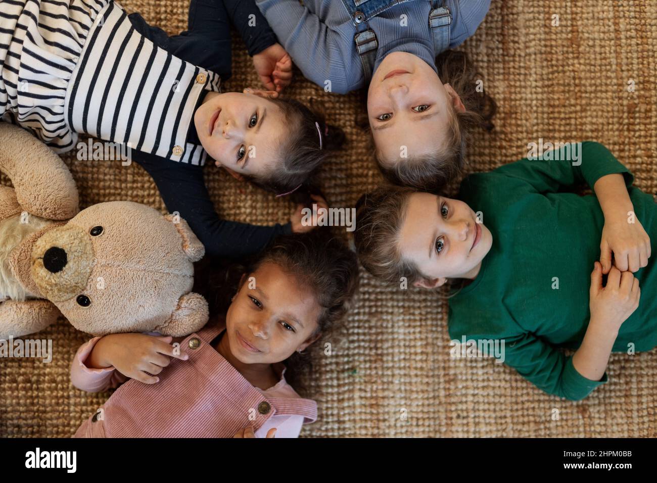 Top view of of little girls friends lying on back on floor and looking at camera. Stock Photo