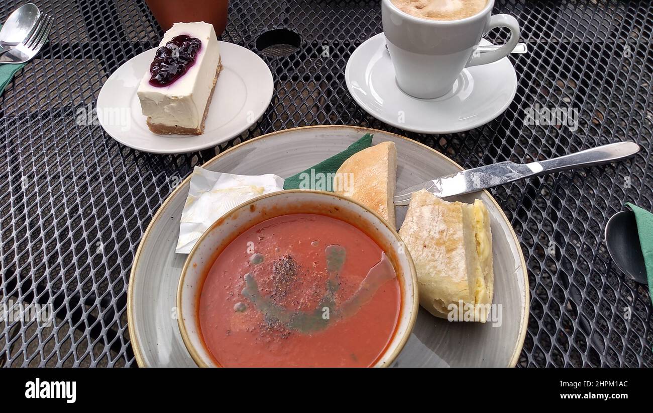 BEETHAM. CUMBRIA. ENGLAND. 08-22-21. An outdoor table at a cafe with a bowl of  tomato soup, portion of cheesecake and a cup of coffee. Stock Photo