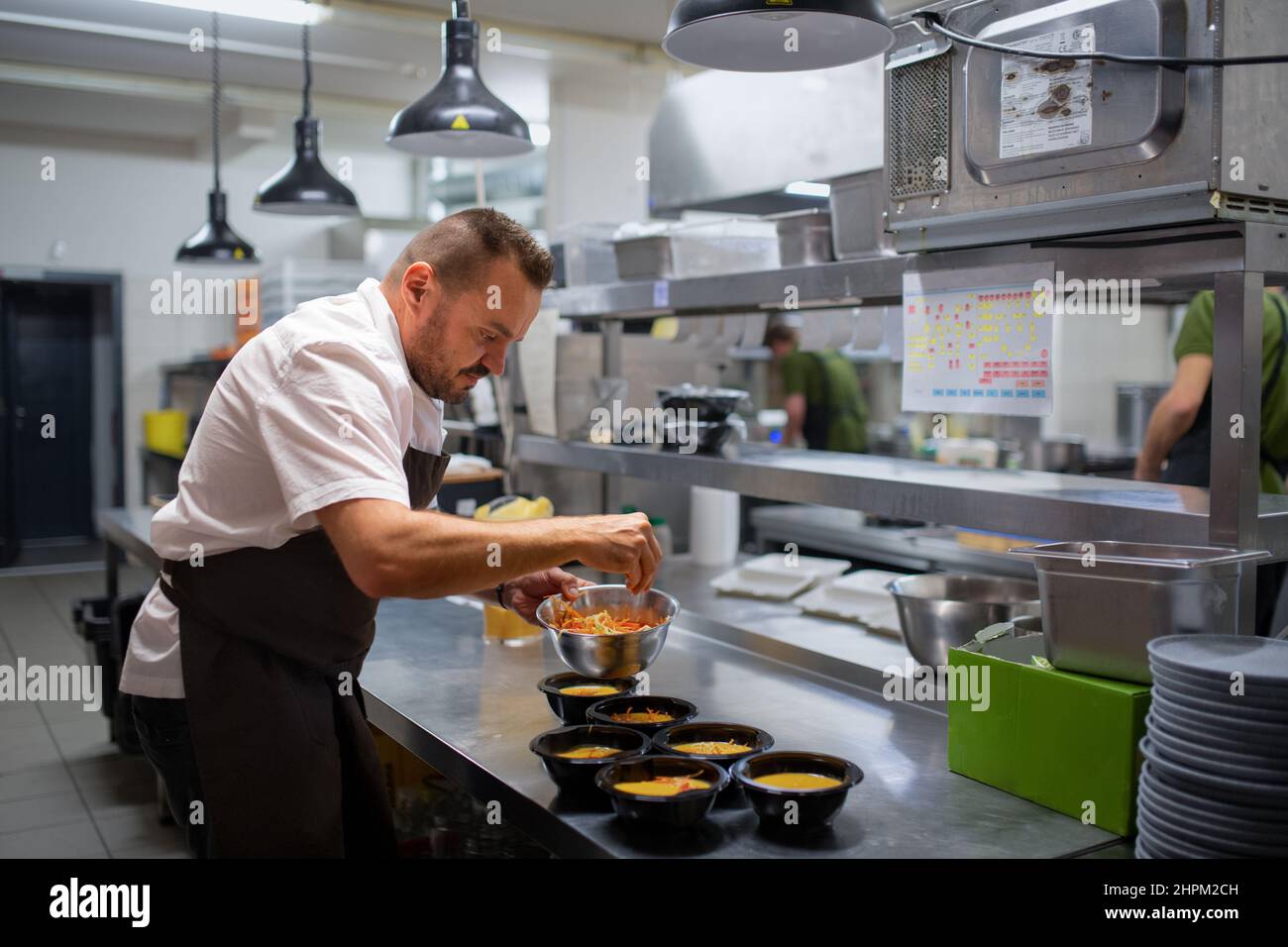 Chef decorating soups in takeaway bowls indoors in restaurant kitchen. Stock Photo