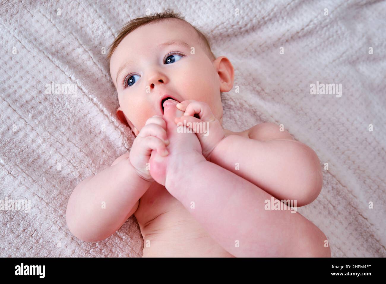 Portrait of a happy infant baby on the bed pulling his leg into his