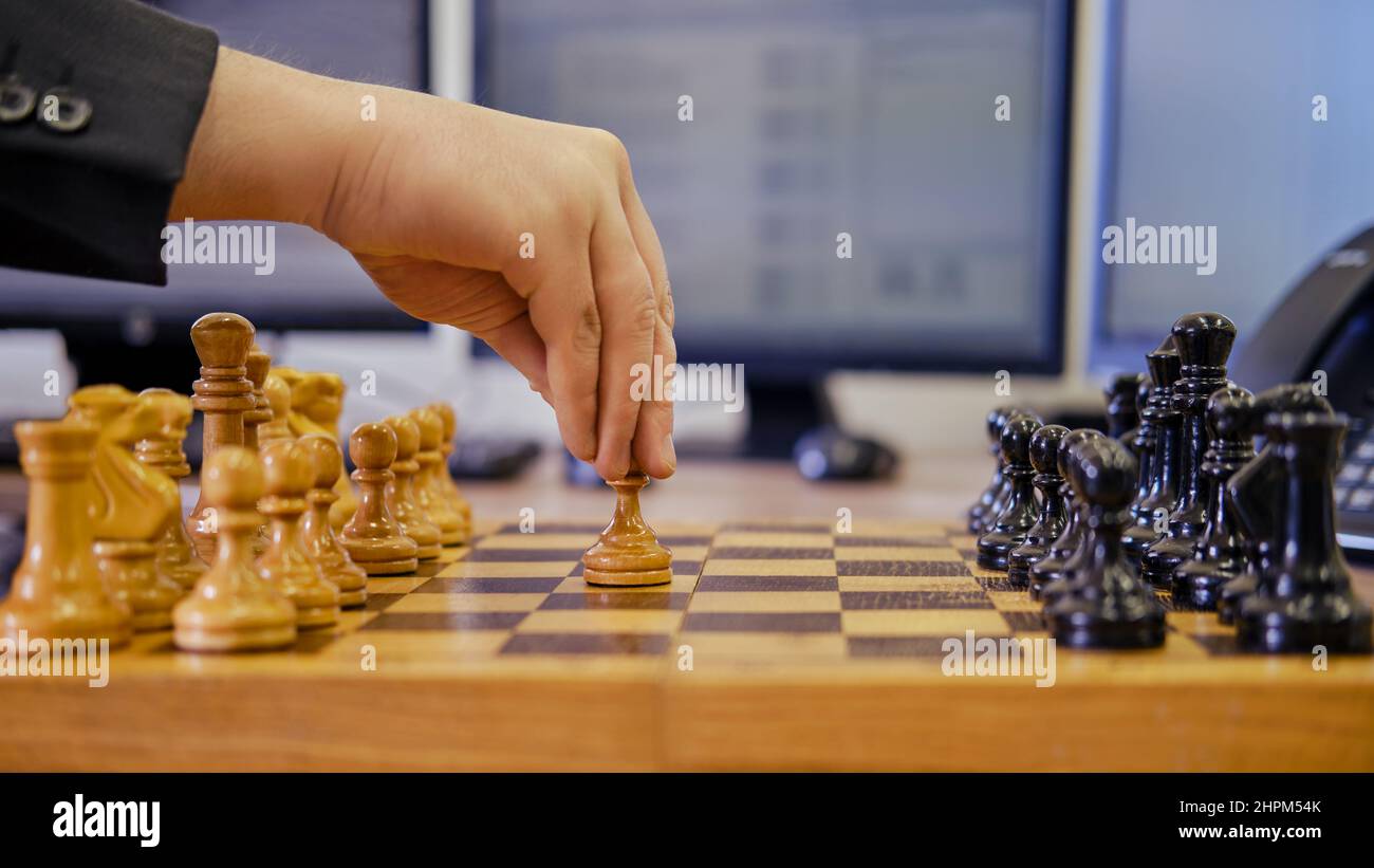 A businessman man with a chess piece pawn in his hands is working on a computer keyboard at an office desk, close-up Stock Photo