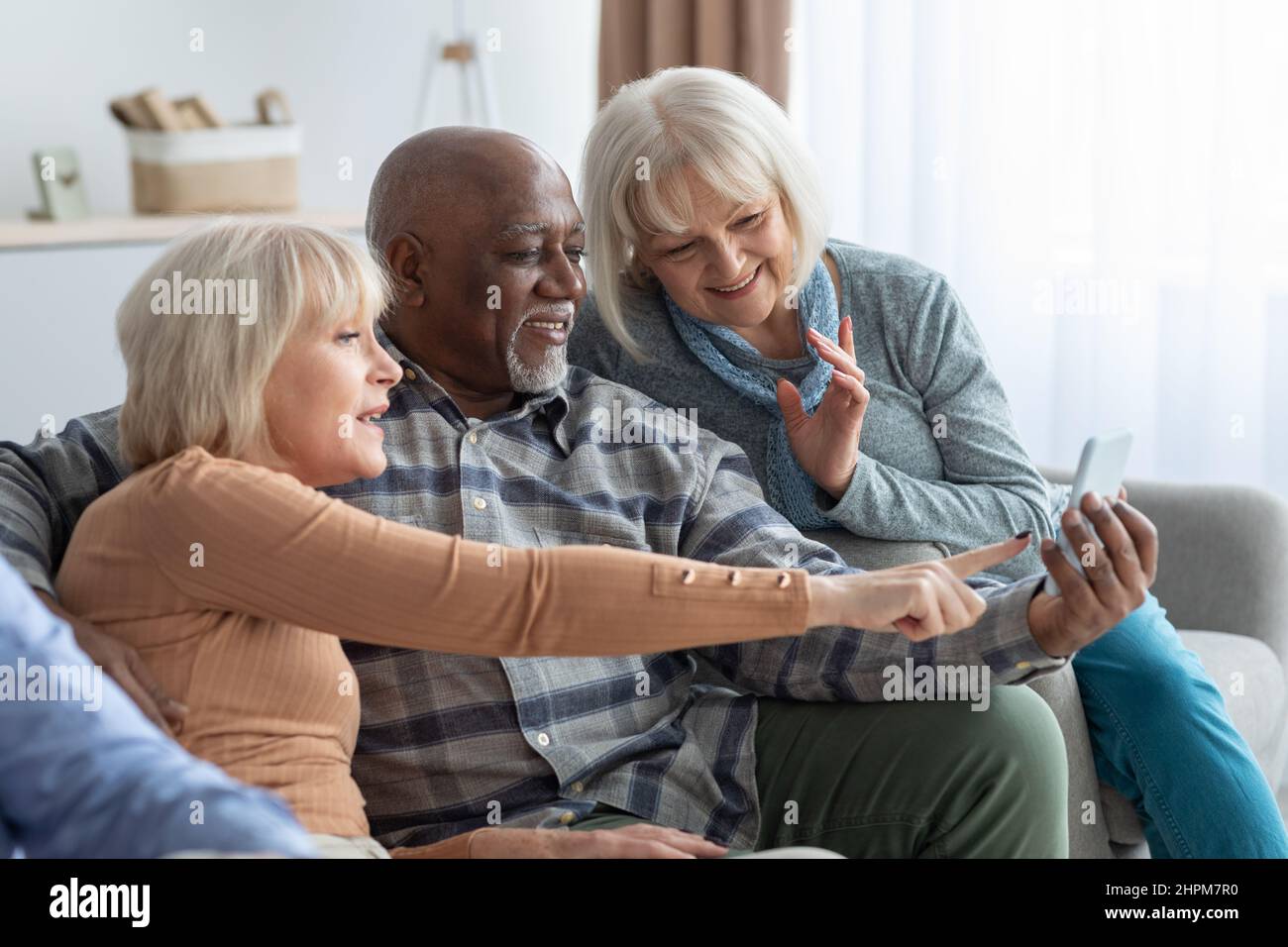 Cheerful elderly people spending time together at home, using smartphone Stock Photo