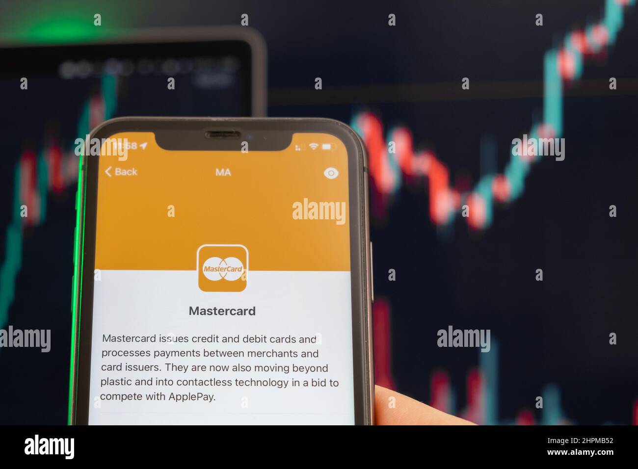 Mastercard stock price increasing on the trading market with uptrend line graph bar chart on the background. Man holding a mobile phone with company logo, February 2022, San Francisco, USA Stock Photo