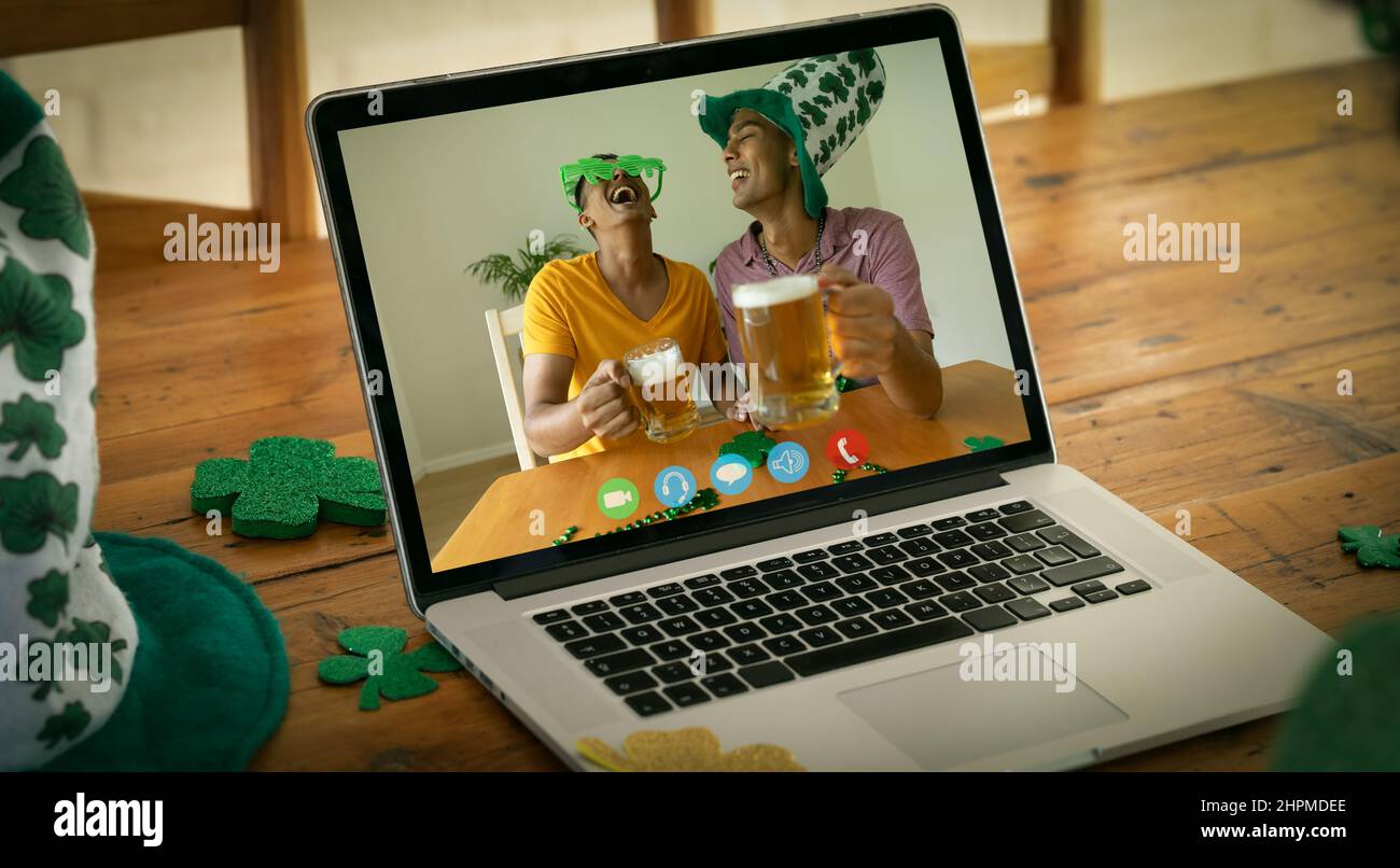 Two mixed race male friends with beers making st patrick's day video call on laptop screen at home Stock Photo