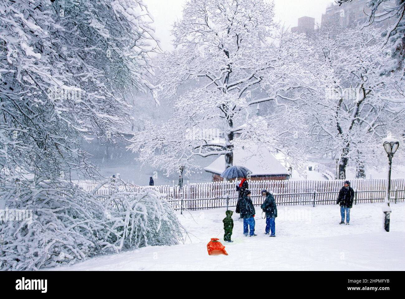 Central Park snow New York scenic. Heavy snowfall. People next to boat pond or boat basin enjoying the winter weather landscape. Child and red sled Stock Photo