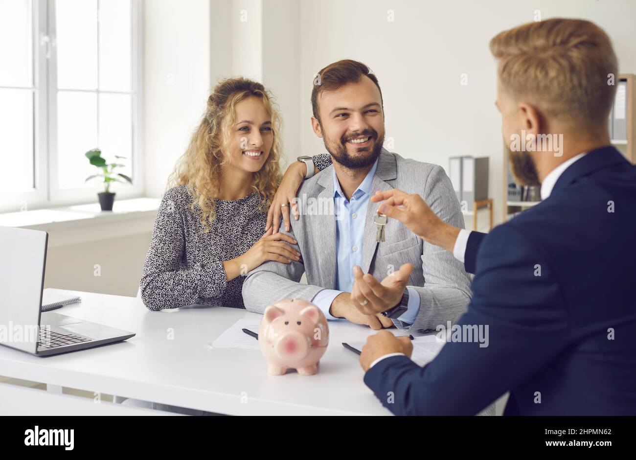 Happy young family signs contract in office and receives keys from real estate agent. Stock Photo