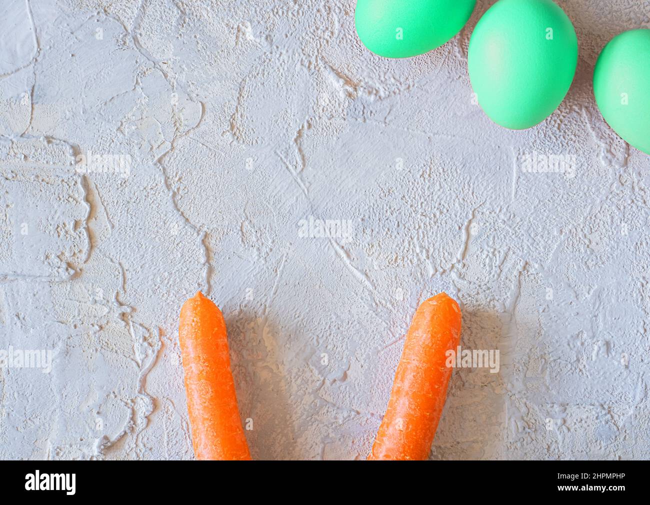 easter colored eggs with bunny carrot ears on light textured background. Stock Photo