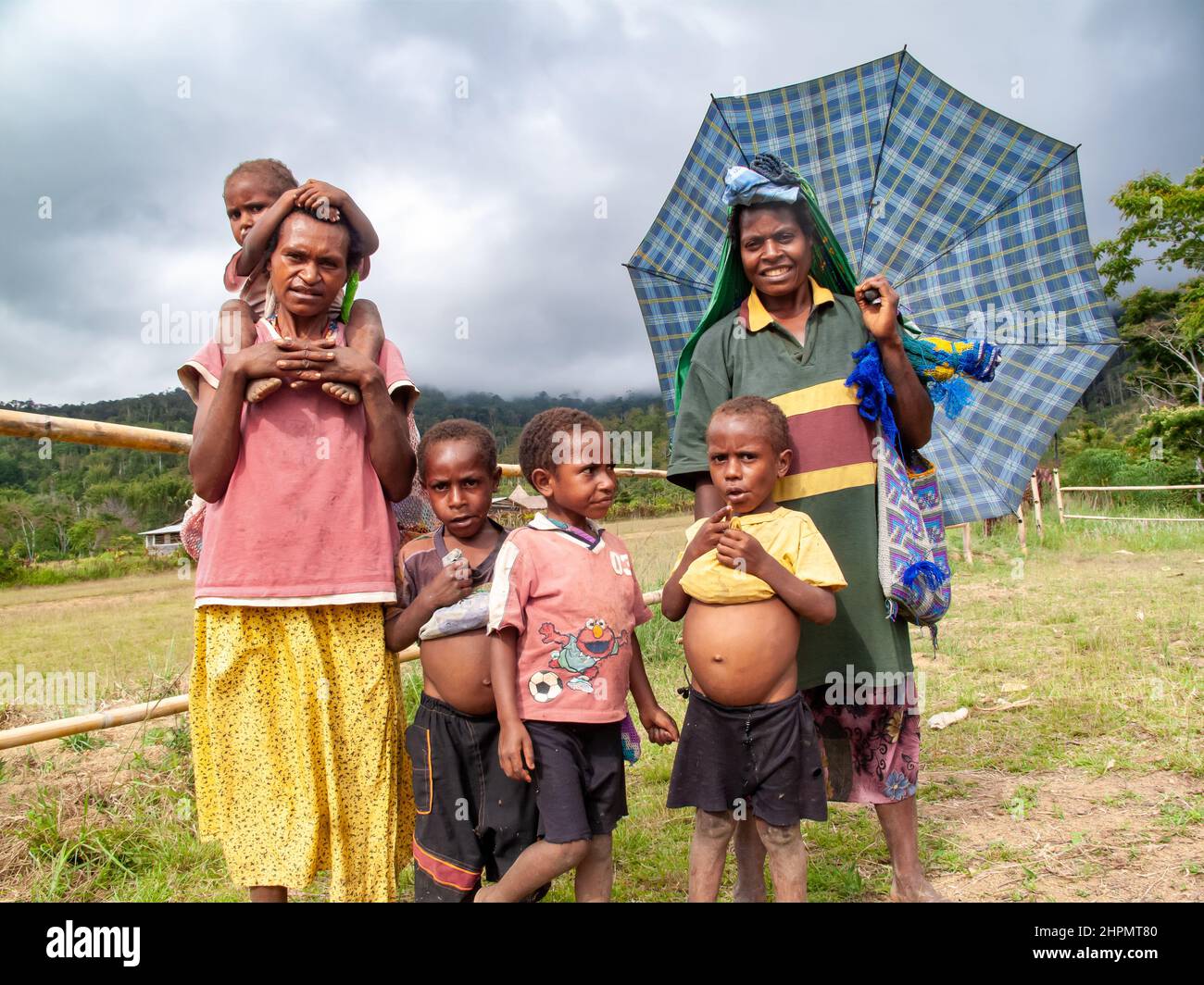Two women and four children in highland PNG. Two boys have shirts pulled up showing enlarged bellies from either kwashiorkor or splenomegaly. Stock Photo