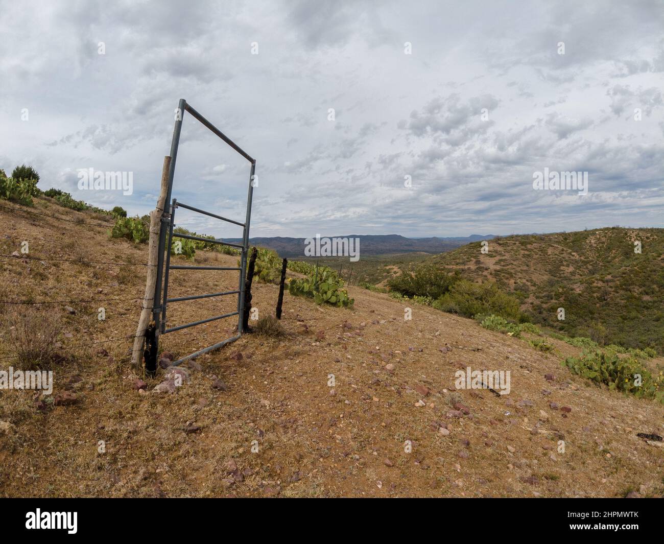 Old livestock gate with barb wire fence in a hilly, desert landscape on a cloudy day. Stock Photo