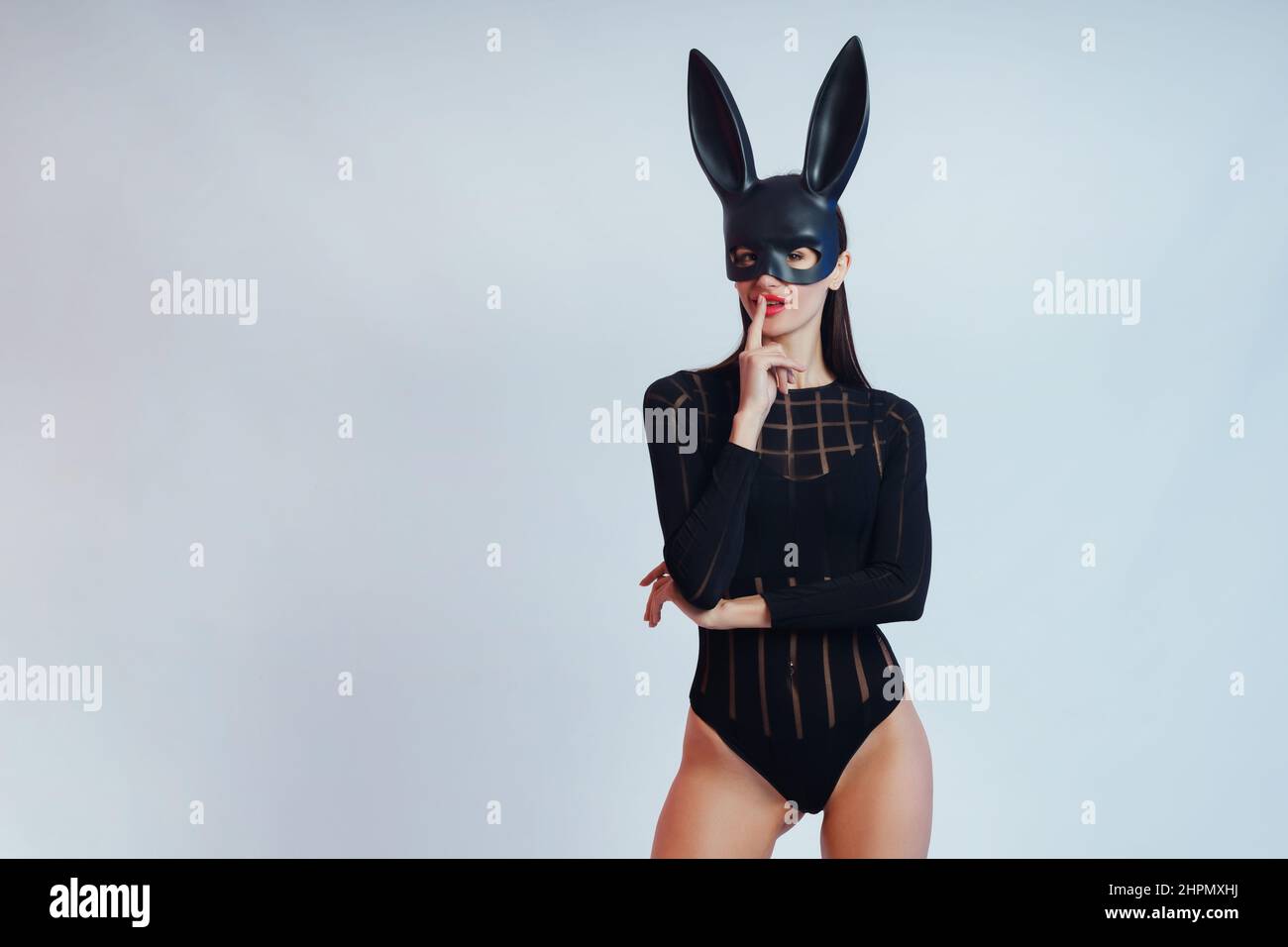Sexy woman wearing a black mask Easter bunny standing on a blue background and looks very sensually. Stock Photo