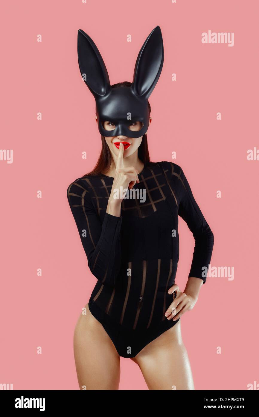 Sexy woman wearing a black mask Easter bunny standing on a pink background and looks very sensually. Stock Photo