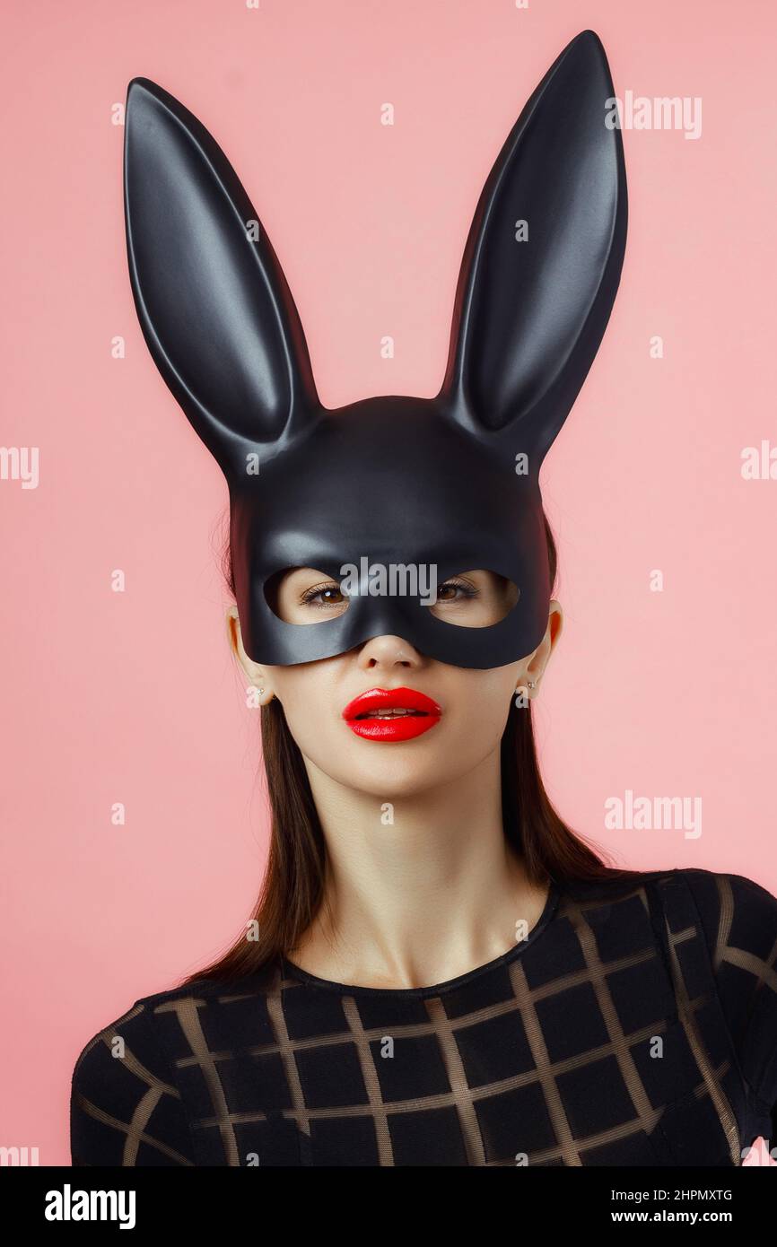 Sexy woman wearing a black mask Easter bunny standing on a pink background and looks very sensually. Stock Photo