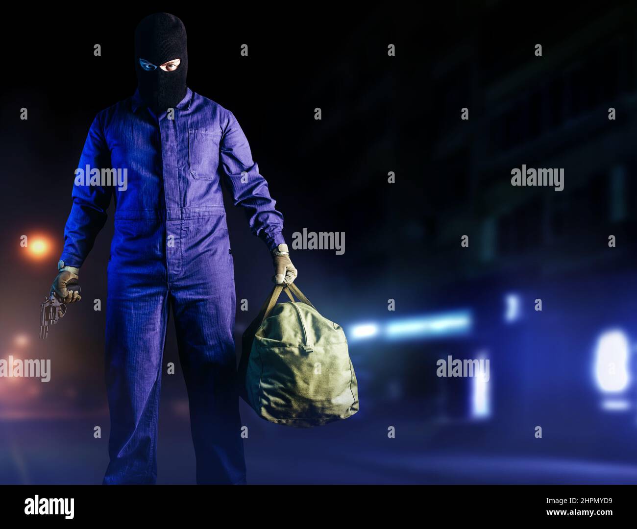 Photo of robber in mask, overalls, gloves, bag and gun standing front view on night street background. Stock Photo