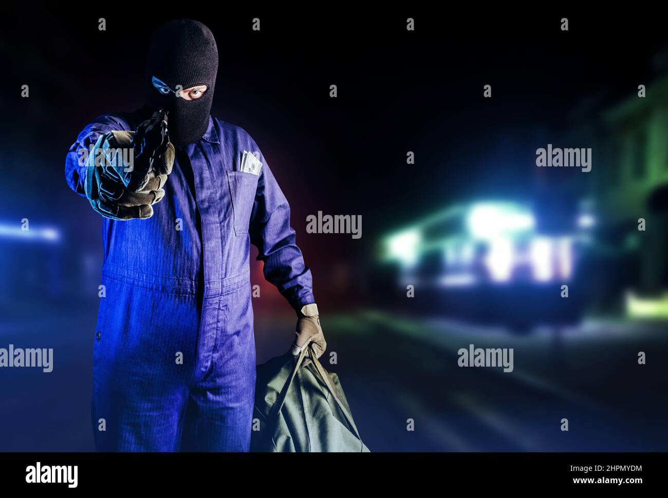 Photo of robber in mask, overalls, gloves, bag and gun standing front view and aiming on night street background. Stock Photo