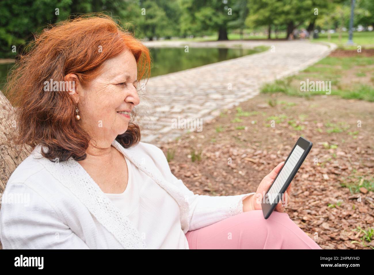 Mature hispanic woman reading an ebook on an electronic reader sitting in a park. Concepts: technology and reading. Image with copy space Stock Photo
