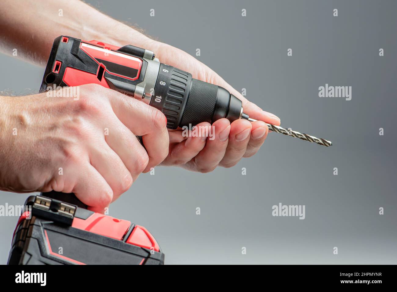 The man's hands install the drill into the drill, the hands take the drill and install it into the electric drill. Cordless tool on a gray background Stock Photo