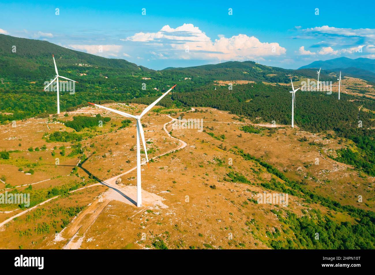 Rotating wind driven generators produce alternative energy scattered in highland against forestry mountains protecting environment aerial view Stock Photo