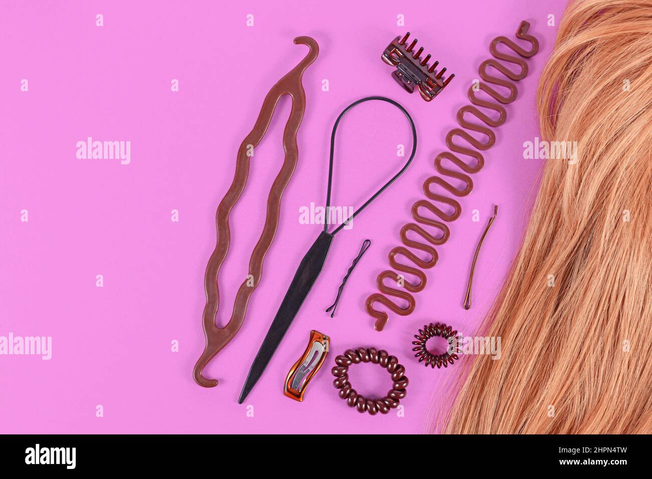 Set of hair styling tools like bun maker, braid tool, ponytail style maker, hair clip, rubber bands and pins next to blond hair with copy space Stock Photo