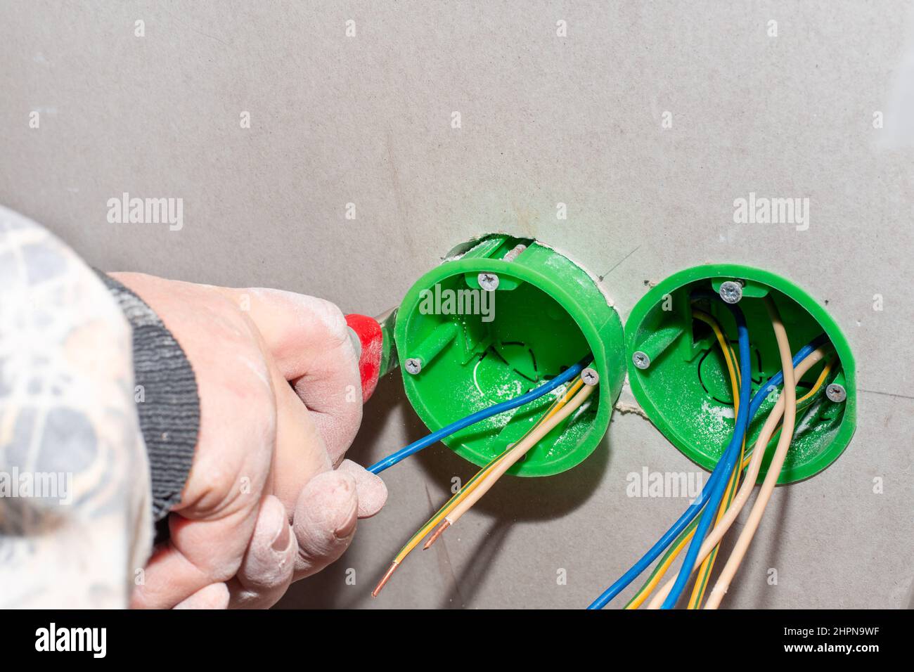 An electrician installs an outlet box into a drywall wall to install an